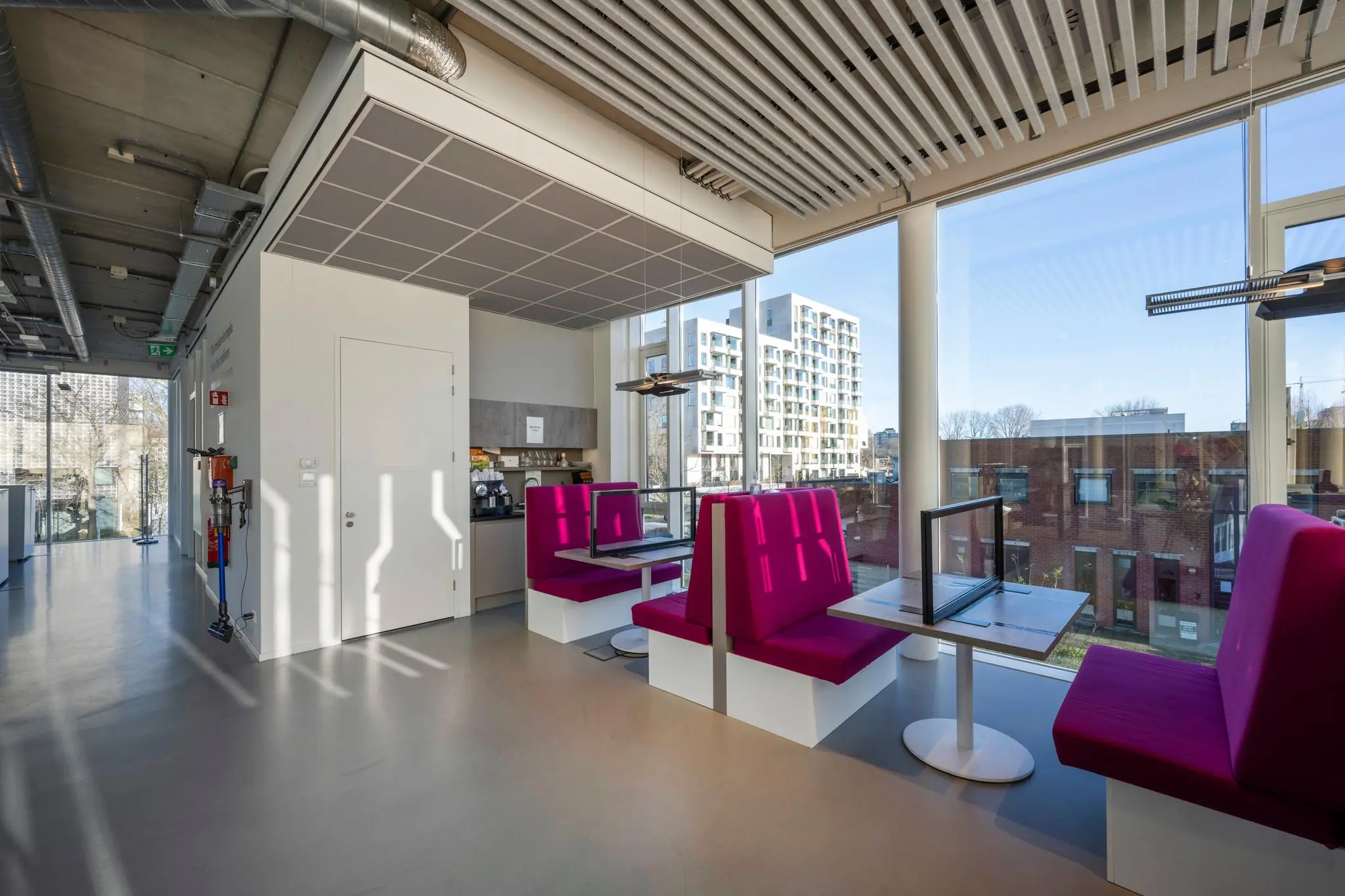 Moderne kantineruimte aan de Fred. Roeskestraat met paarse zitbanken, grote ramen en uitzicht op omliggende gebouwen.